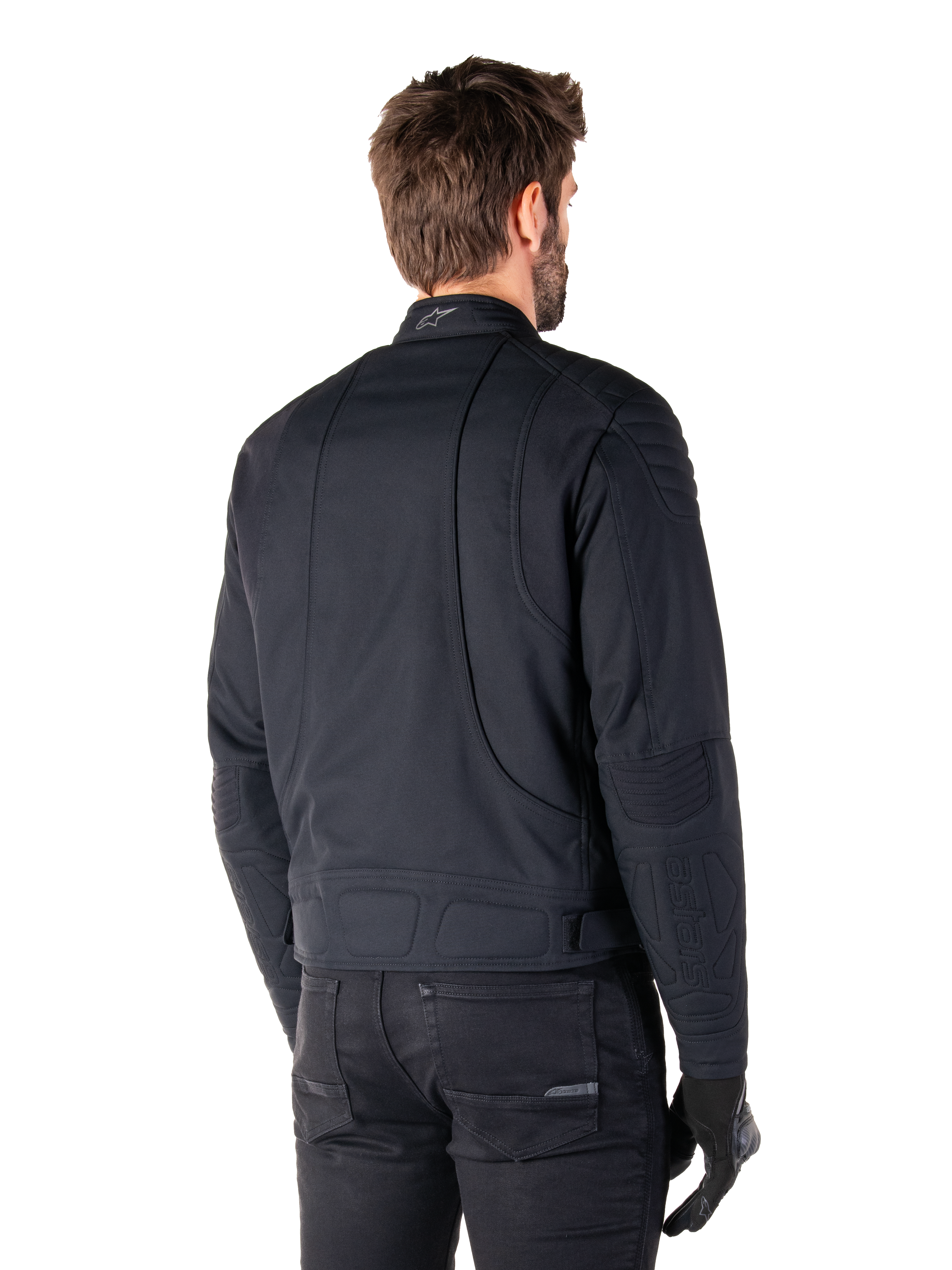 Alpinestars Clayton WR Jakke i sort, trekvart visning bagfra på en mandlig model, urban motorcykeljakke med quiltet polstring på skuldre og albuer, tekniske syninger og reflekterende logo på kraven, stylet med sorte bukser og handsker.