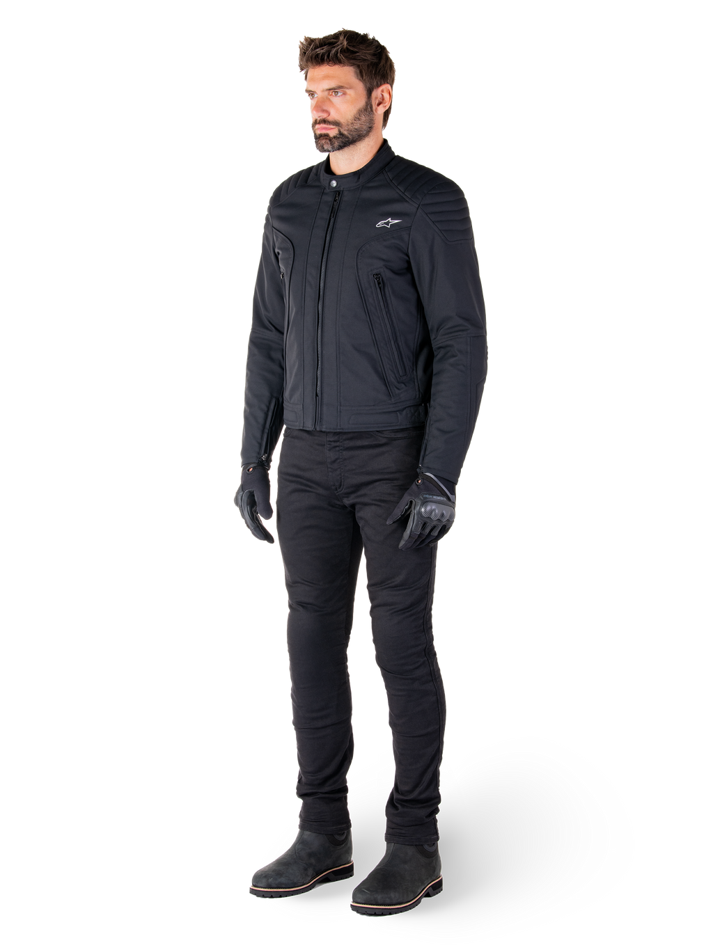 Mandlig kører iført Alpinestars Clayton WR-jakken, sort urban motorcykeljakke, slim-fit design med quiltede skulderdetaljer og mat finish, kombineret med sorte tekniske kørebukser og handsker.