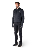 Mandlig kører iført Alpinestars Clayton WR-jakken, sort urban motorcykeljakke, slim-fit design med quiltede skulderdetaljer og mat finish, kombineret med sorte tekniske kørebukser og handsker.