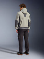 Mandlig model set bagfra iført Alpinestars Moblast Waterproof Jacket i Iron Gray Dark Sage, urban motorcykeljakke med hætte, mørkegrå sidepaneler og forstærkede albuelapper, kombineret med mørke kørebukser og sorte sneakers, moderne minimalistisk æstetik til urban pendling