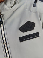Alpinestars Moblast vandtæt jakke, Iron Gray, nærbillede af brystmærker med Alpinestars-logo og MO.ST.EQ. Moto Streetwear Equipment-branding, teknisk ripstop-materiale med kraftig lynlås foran og detalje på skulderlomme