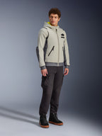 Alpinestars Moblast vandtæt jakke, Iron Gray og Dark Sage, urban motorcykeljakke med hættetrøjedesign, båret af en model med mørke kørebukser og sorte støvler, minimalistisk cyber-tech-æstetik med gult indvendigt for i hætten og vandtætte lynlåse