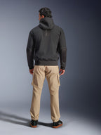 Alpinestars Moblast vandtæt jakke, sort, urban motorcykel-hættetrøje set bagfra, båret med sandfarvede cargobukser og sorte sneakers, minimalistisk design med lodret 'astars'-branding på den øverste del af ryggen, moderne køreudstyr til al slags vejr