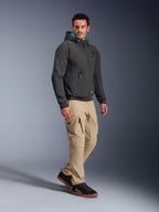 Mandlig model iført Alpinestars Moblast Waterproof Jacket i sort, urban motorcykel-hættetrøje med teal-farvet for i hætten, kombineret med khaki cargobukser og sorte sneakers, moderne minimalistisk design med teknisk strækstof til pendling i al slags vejr