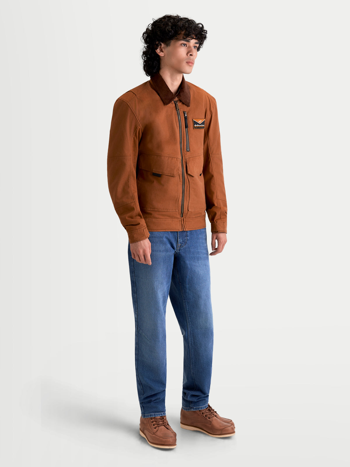 Alpinestars Mustang WP jakke, herre-motorcykeljakke i mørk rust og mørkebrun, sideprofilvisning på model iført tekstiludstyr i arbejdstøjsstil og blå jeans