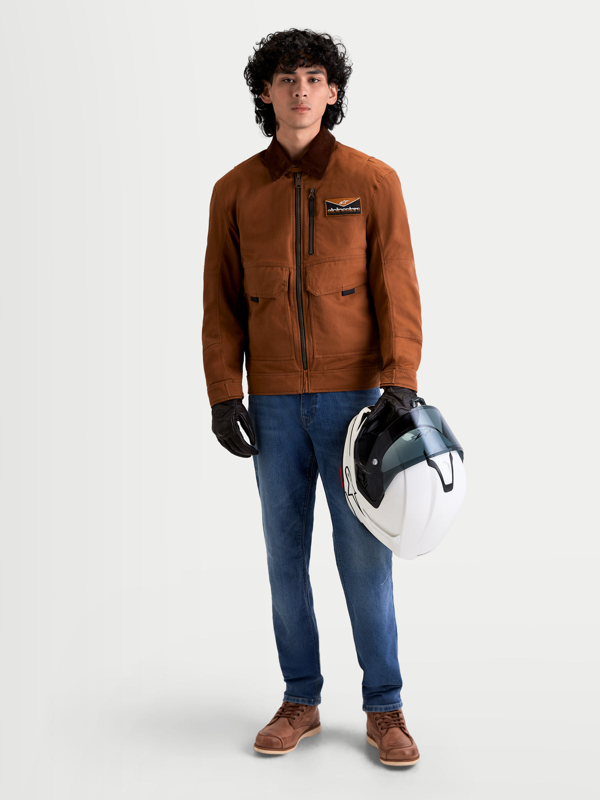 Alpinestars Mustang Waterproof Jacket, men's urban contemporary textile motorcycle jacket in dark rust and dark brown, front view of a model wearing workwear-styled riding gear and holding a white helmet