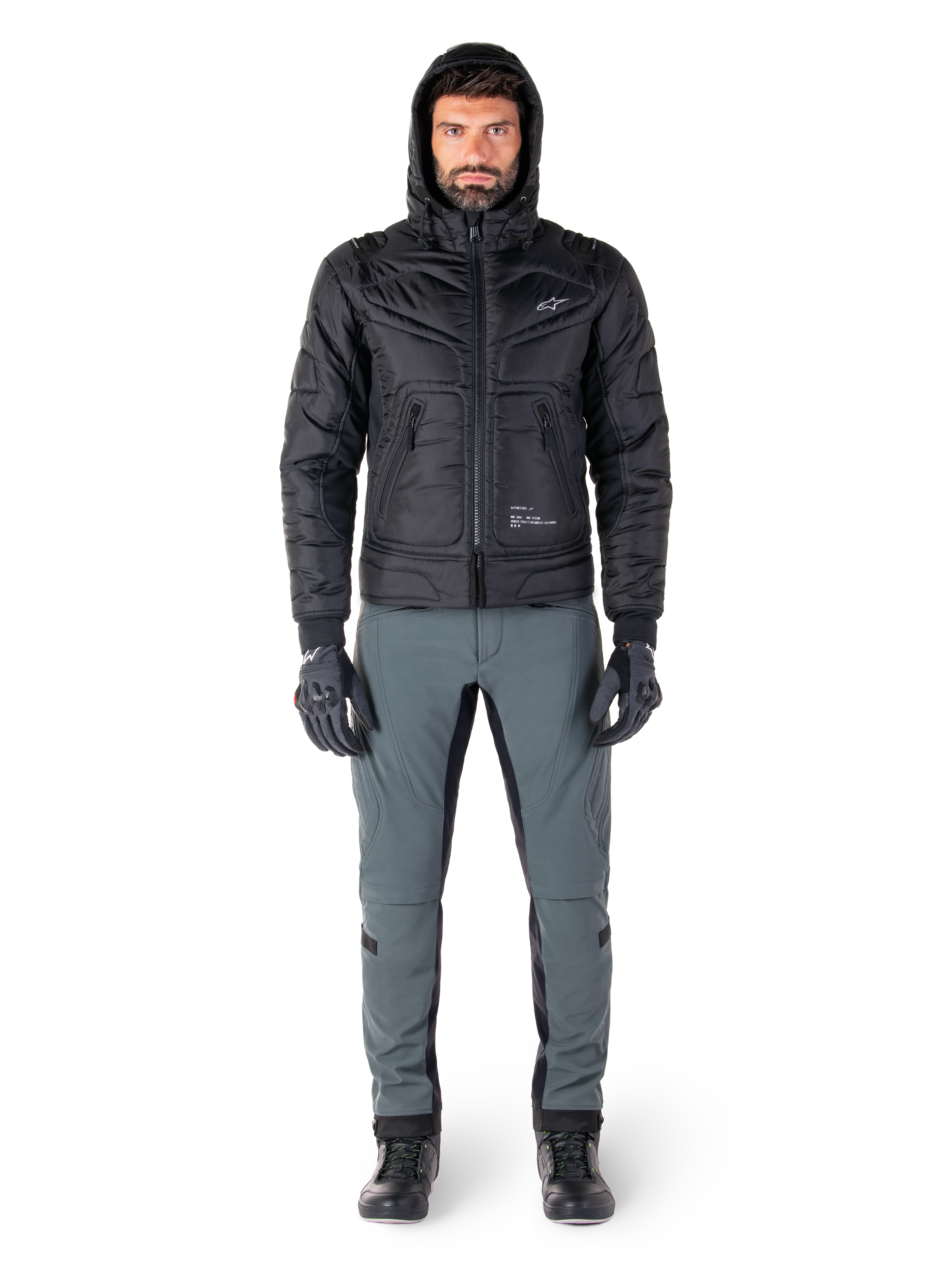 Alpinestars Mohobbs Waterproof-jakke i sort, mandlig model iført quiltet, polstret bomberjakke med hætte, kombineret med grå kørebukser, sorte handsker og sorte støvler, moderne urbant motorcykeludstyr