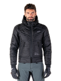 Alpinestars Mohobbs vandtæt jakke, sort polstret bomber-motorcykeljakke, quiltet poly-materiale med lynlås foran og lynlåslommer, lille hvidt logo på brystet, båret af en model med grå bukser og handsker, urban streetwear-design til bykørsel