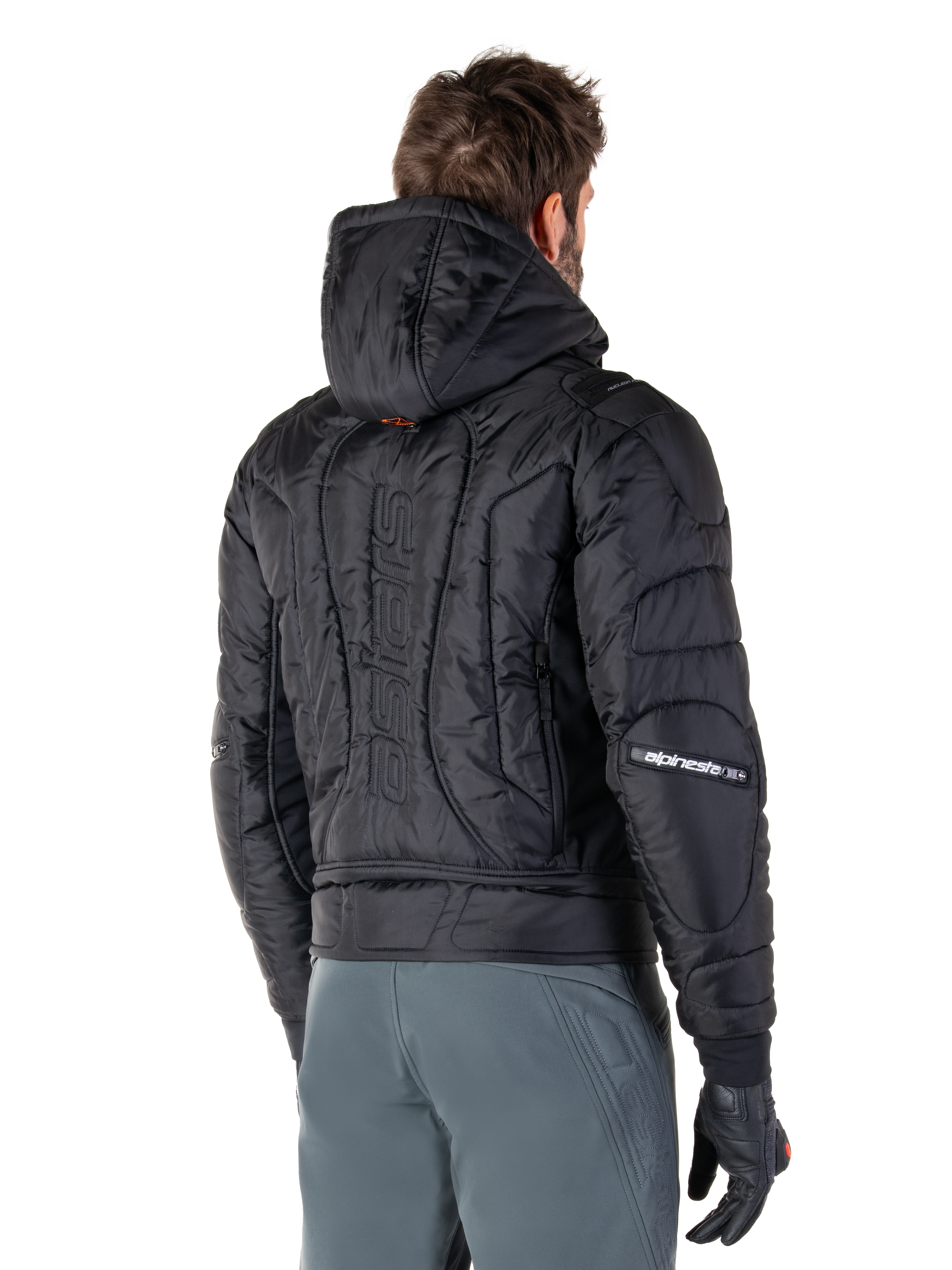 Alpinestars Mohobbs vandtæt jakke, sort, set bagfra med quiltet polstret konstruktion, hætte, lodret astars-ordmærke på ryggen, Alpinestars-branding på ærmerne, båret med grå bukser og sorte handsker