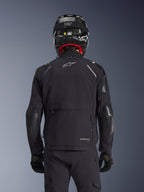 Alpinestars Andes Pro Drystar® XF-jakke i sort, set bagfra på en rytter iført kulfiberhjelm, med et stort opbevaringsrum bagpå og hvidt Alpinestars-logo, teknisk adventure-motorcykeludstyr til hele året.