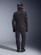 Alpinestars Andes Pro Drystar® XF-jakke i sort og mørkegrå, set bagfra af en rytter i fuldt adventure touring-udstyr, inklusiv matchende bukser og kulfiberhjelm, stor baglomme og reflekterende Alpinestars-branding på ryggen.