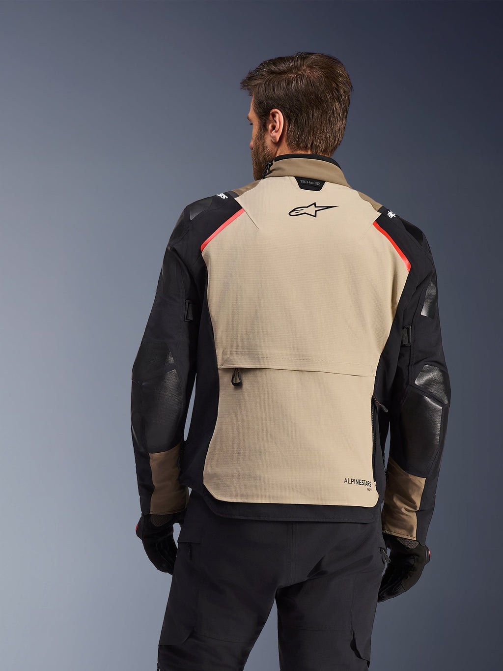 Alpinestars Andes Pro Drystar® XF jakke, set bagfra, Walnut og Aluminum, med et stort sandfarvet rygpanel med sort Alpinestars-logo og røde skulderdetaljer, stor cargo-lomme bagpå, bæres med sorte bukser og handsker, adventure touring motorcykeludstyr
