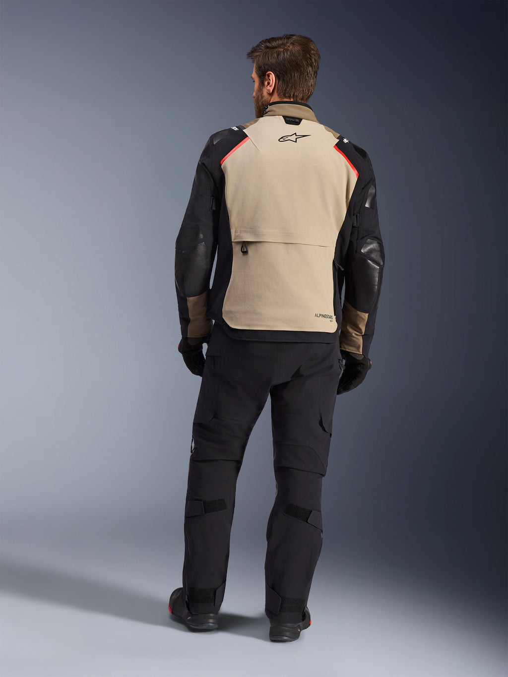 Alpinestars Andes Pro Drystar® XF jakke, Walnut Aluminum, set bagfra, motorcykel adventure-jakke med sorte ærmer og røde skulderdetaljer, båret med sorte kørebukser og handsker.