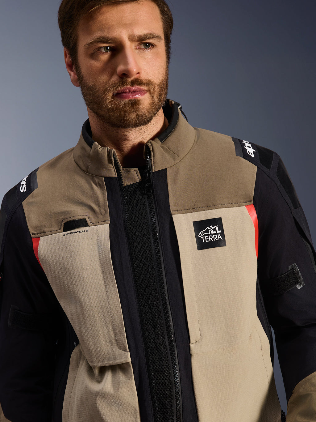 Alpinestars Andes Pro Drystar® XF-jakke i Walnut Aluminum, båret af en mandlig model, adventure-motorcykeljakke med lagdelt tekstildesign i brun, lysegrå og sort med røde detaljer, Alpinestars 'TERRA'-logo på brystet og synlige tekniske detaljer.