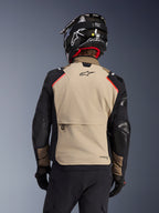 Alpinestars Andes Pro Drystar® XF jakke i Walnut Aluminum, set bagfra, sandfarvet rygpanel med stor cargolomme, sorte ærmer med forstærkede paneler, Alpinestars-logo på den øverste del af ryggen, kombineret med sort hjelm og handsker til adventure touring.