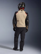 Alpinestars Andes Pro Drystar® XF-jakke set bagfra i farven Walnut Aluminum, sandfarvet rygpanel med sorte ærmer og røde detaljer, kombineret med sorte tekniske adventure-bukser og motorcykelhjelm, premium touring-udstyr til al slags vejr