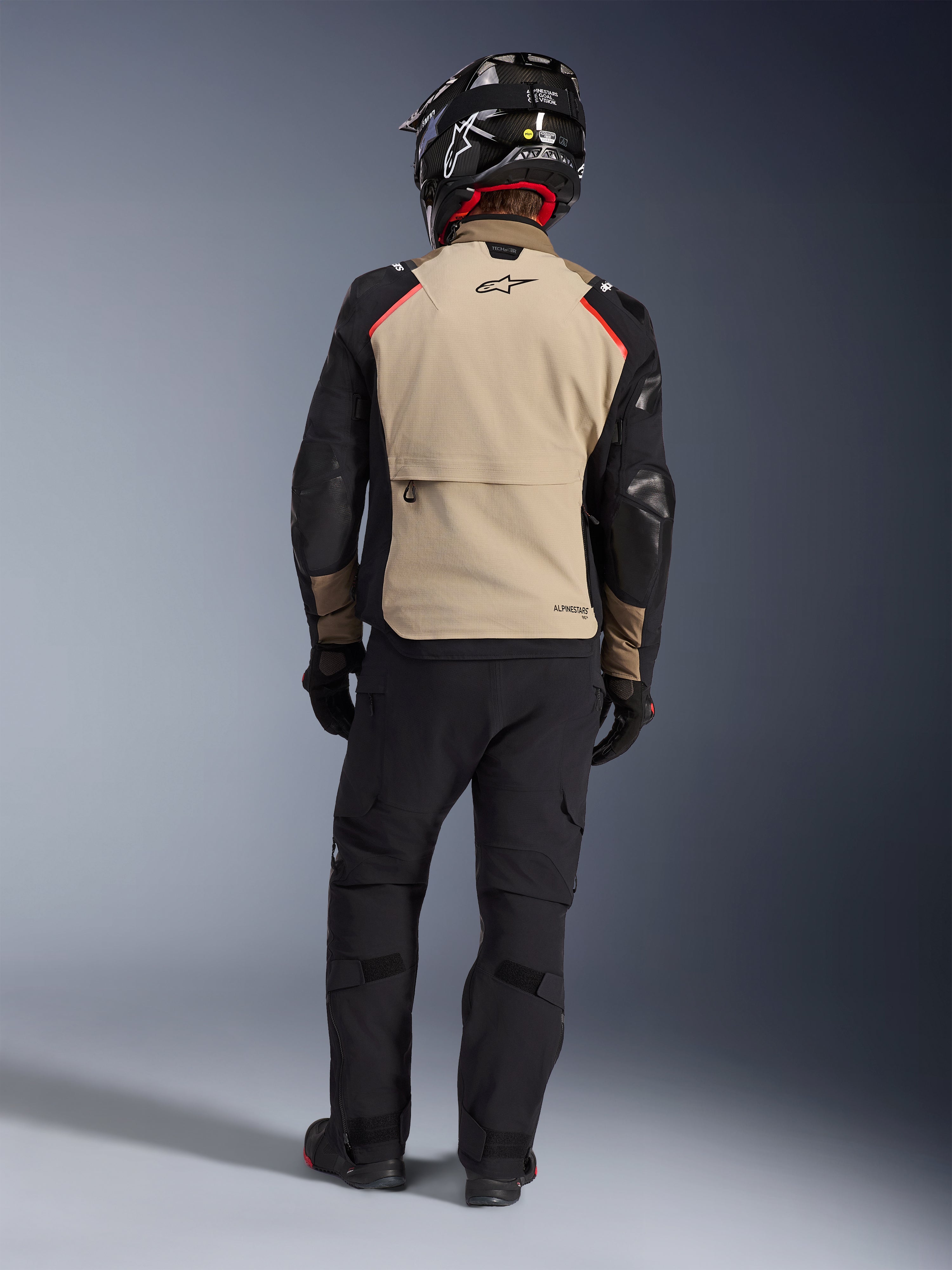 Alpinestars Andes Pro Drystar® XF-jakke set bagfra i farven Walnut Aluminum, sandfarvet rygpanel med sorte ærmer og røde detaljer, kombineret med sorte tekniske adventure-bukser og motorcykelhjelm, premium touring-udstyr til al slags vejr