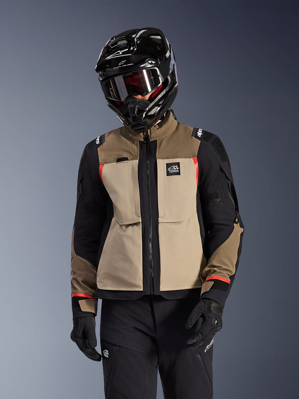 Alpinestars Andes Pro Drystar® XF-jakke, adventure touring-motorcykeljakke, Walnut Aluminum beige og brun med sorte paneler og røde detaljer, båret med en sort Alpinestars-hjelm og goggles, teknisk udendørs motorcykeludstyr
