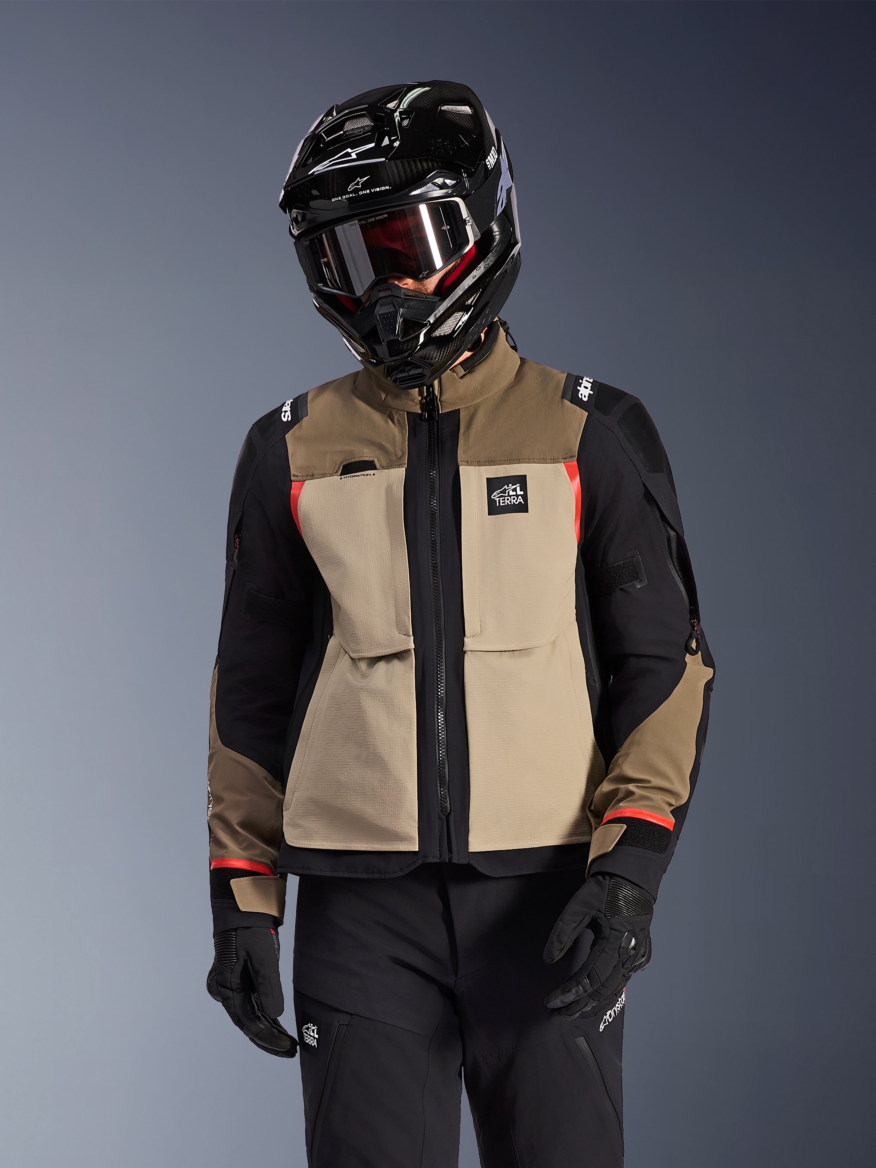 Alpinestars Andes Pro Drystar® XF-jakke, adventure touring-motorcykeljakke, Walnut Aluminum beige og brun med sorte paneler og røde detaljer, båret med en sort Alpinestars-hjelm og goggles, teknisk udendørs motorcykeludstyr