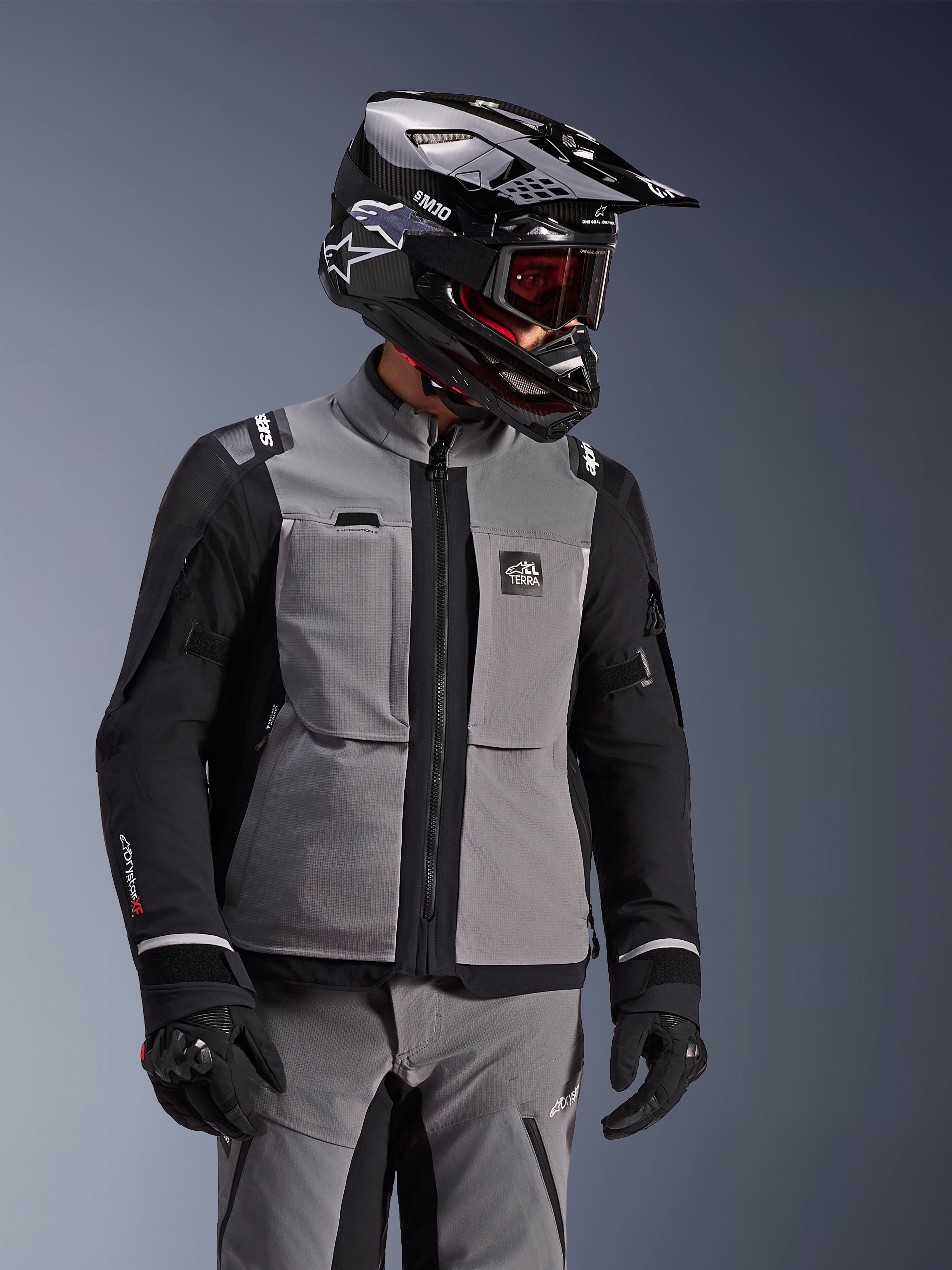 Alpinestars Andes Pro Drystar® XF jakke, mørkegrå og sort, adventure-motorcykeljakke båret med sort SM10-hjelm og matchende køreudstyr, 3-lags tekstildesign med central lynlås og brystlommer, leddelt design til touring i al slags vejr