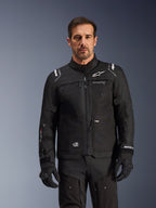 Alpinestars Cusco Drystar® jakke, sort motorcykeljakke, båret af en model med matchende sorte handsker og bukser, teknisk tekstilkonstruktion med hvide Alpinestars-logoer, designet til road adventure touring