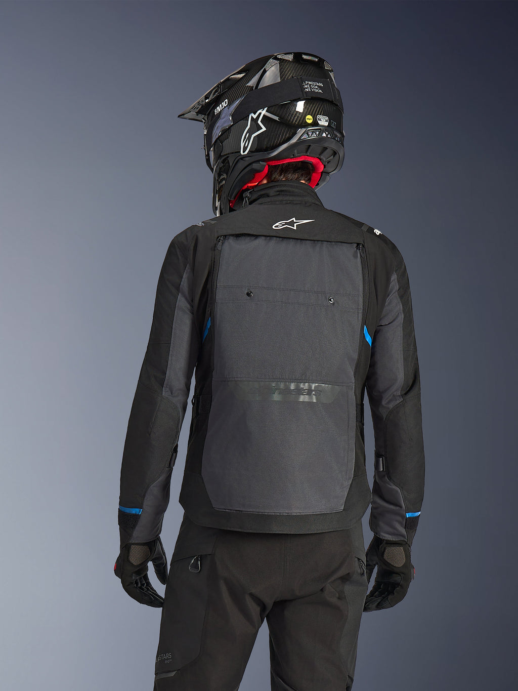 Motorcyklist set bagfra iført Alpinestars Cusco Drystar®-jakke i sort og mørkegrå, med et stort gråt ventilationspanel på ryggen og hvidt logo, kombineret med en sort off-road-hjelm og sort køreudstyr til adventure-touring.