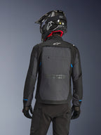 Motorcyklist set bagfra iført Alpinestars Cusco Drystar®-jakke i sort og mørkegrå, med et stort gråt ventilationspanel på ryggen og hvidt logo, kombineret med en sort off-road-hjelm og sort køreudstyr til adventure-touring.