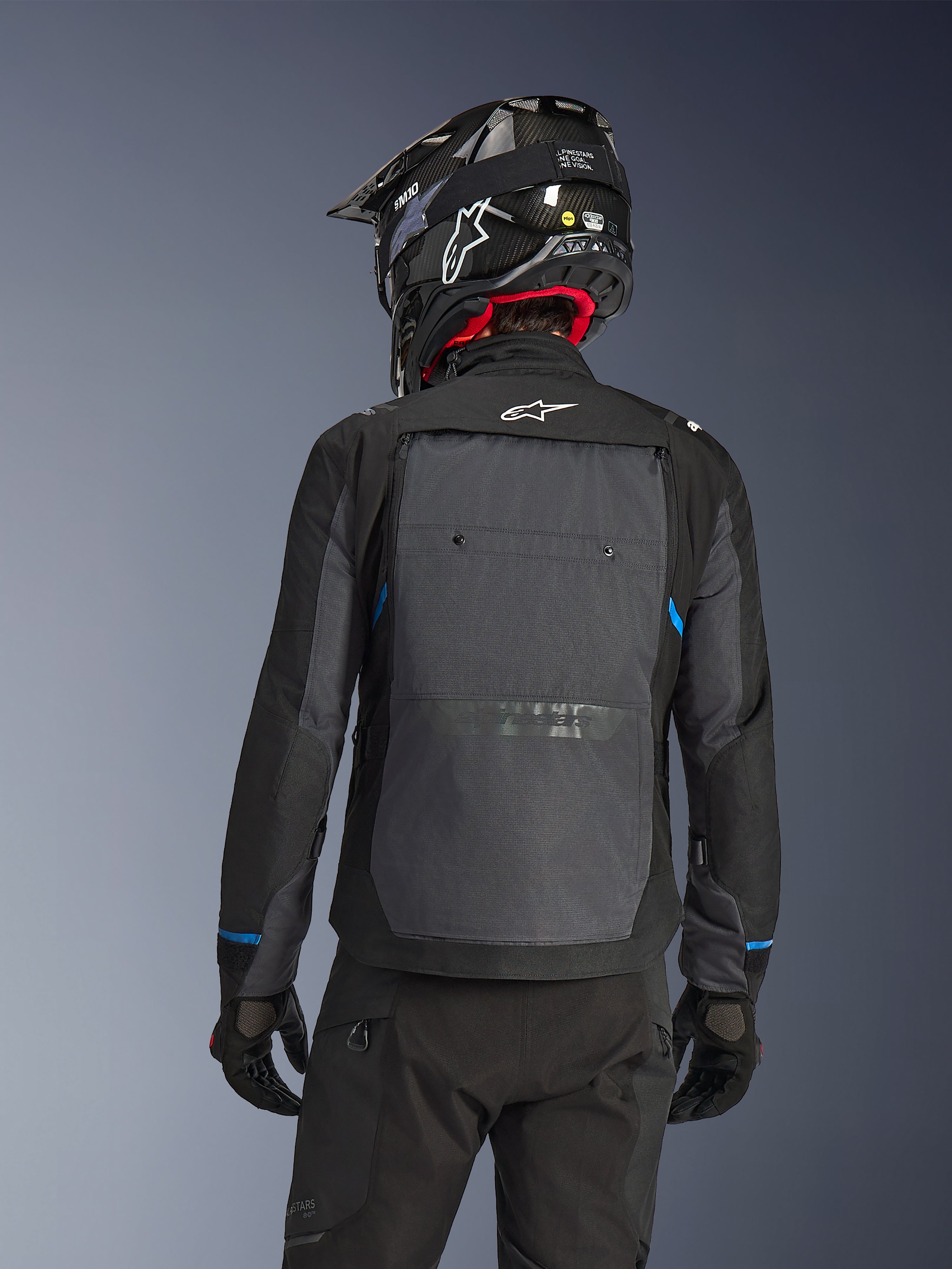 Motorcyklist set bagfra iført Alpinestars Cusco Drystar®-jakke i sort og mørkegrå, med et stort gråt ventilationspanel på ryggen og hvidt logo, kombineret med en sort off-road-hjelm og sort køreudstyr til adventure-touring.