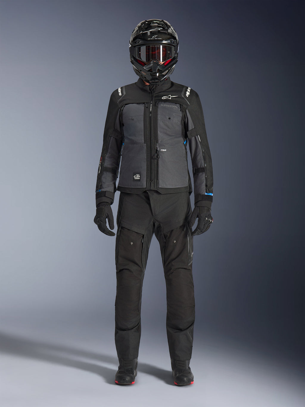 Alpinestars Cusco Drystar® jakke, sort og mørkegrå adventure touring-jakke, båret med matchende sorte bukser, handsker og en full-face hjelm, fuldkropsbillede forfra, beskyttende motorcykelbeklædning