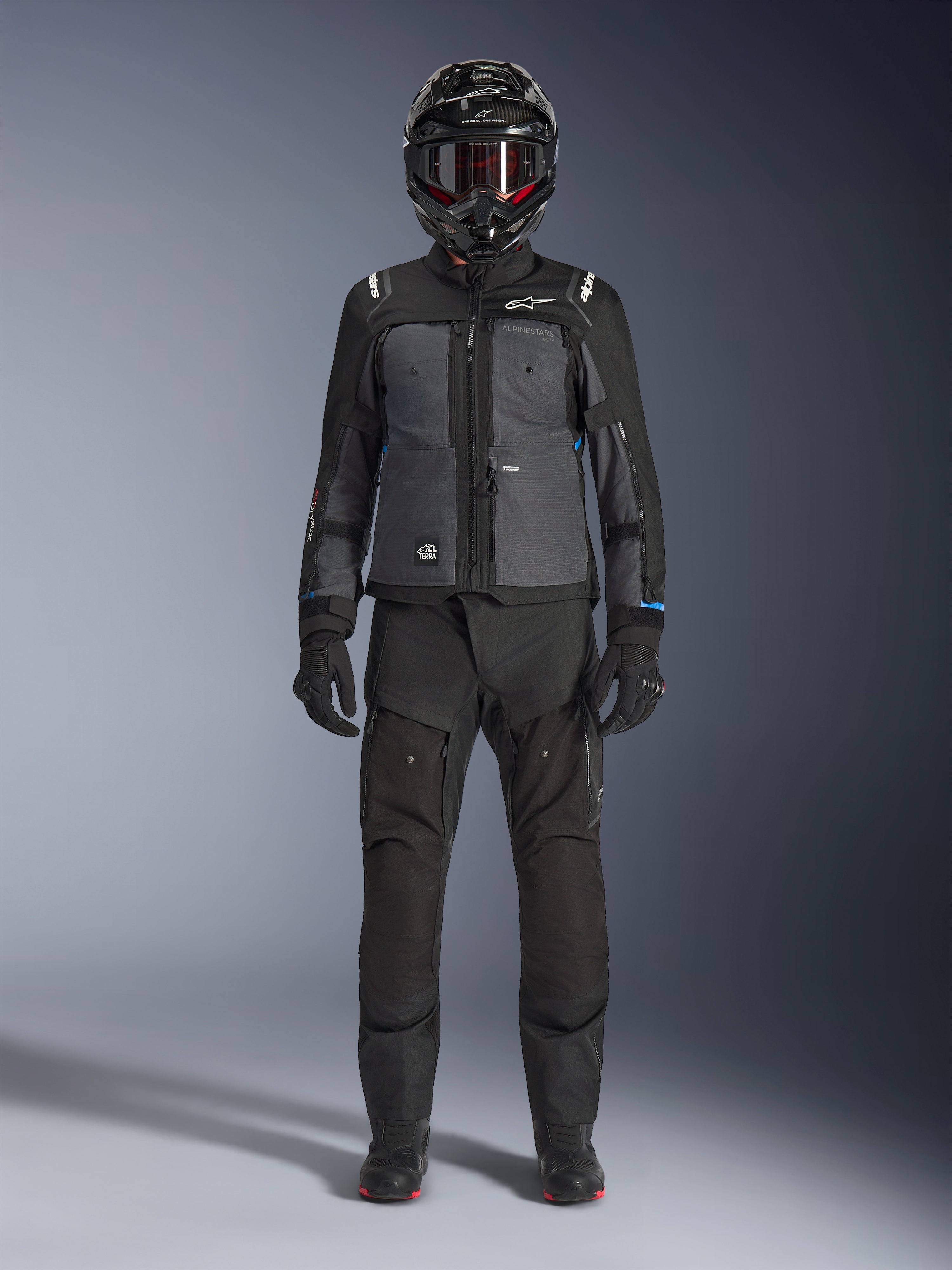 Alpinestars Cusco Drystar® jakke, sort og mørkegrå adventure touring-jakke, båret med matchende sorte bukser, handsker og en full-face hjelm, fuldkropsbillede forfra, beskyttende motorcykelbeklædning