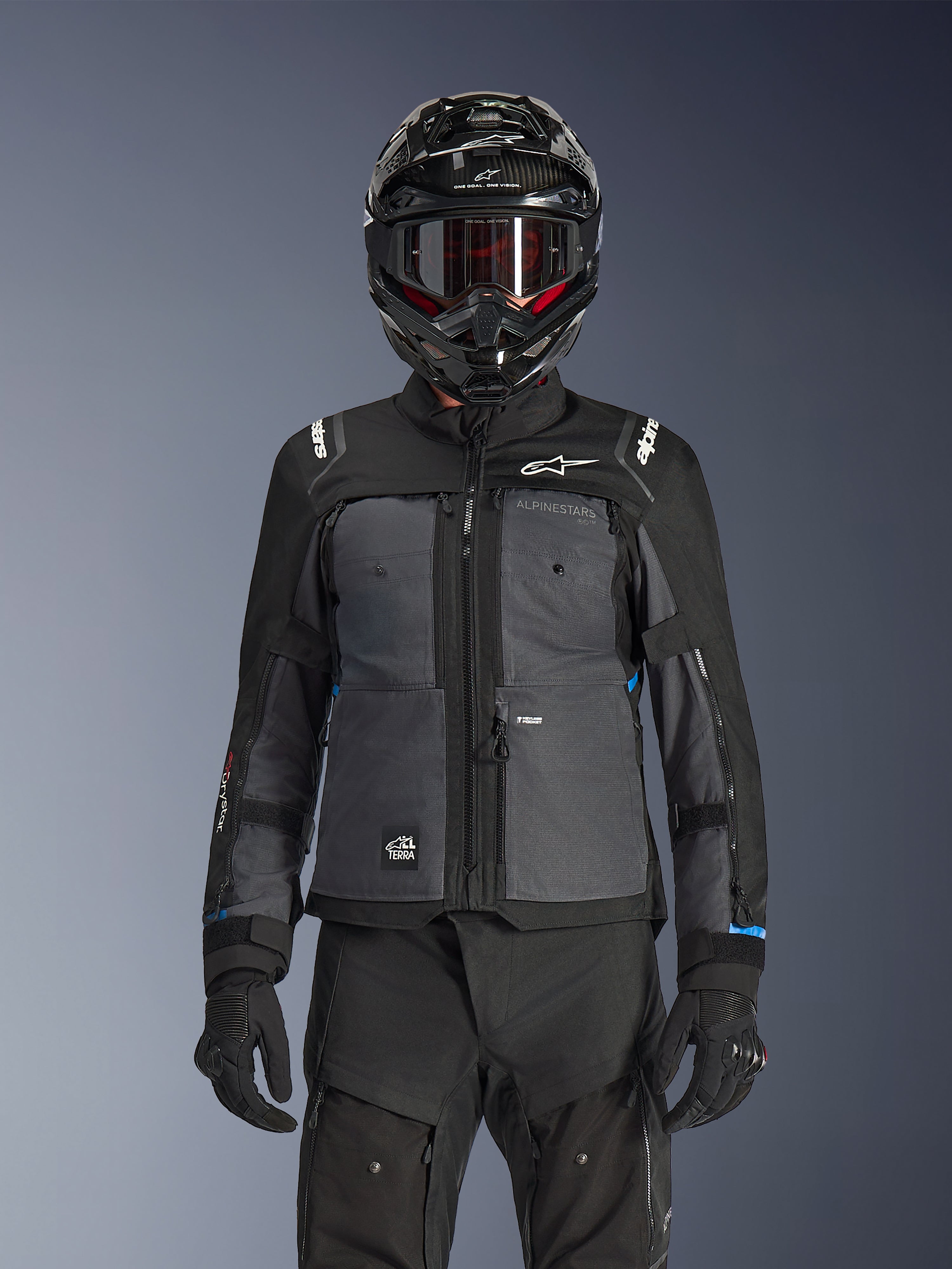 Alpinestars Cusco Drystar® jakke, adventure touring-jakke til motorcykel, sort og mørkegrå, båret med matchende sorte tekniske bukser og en dual-sport-hjelm, med et tofarvet design med ripstop-paneler og Alpinestars-branding