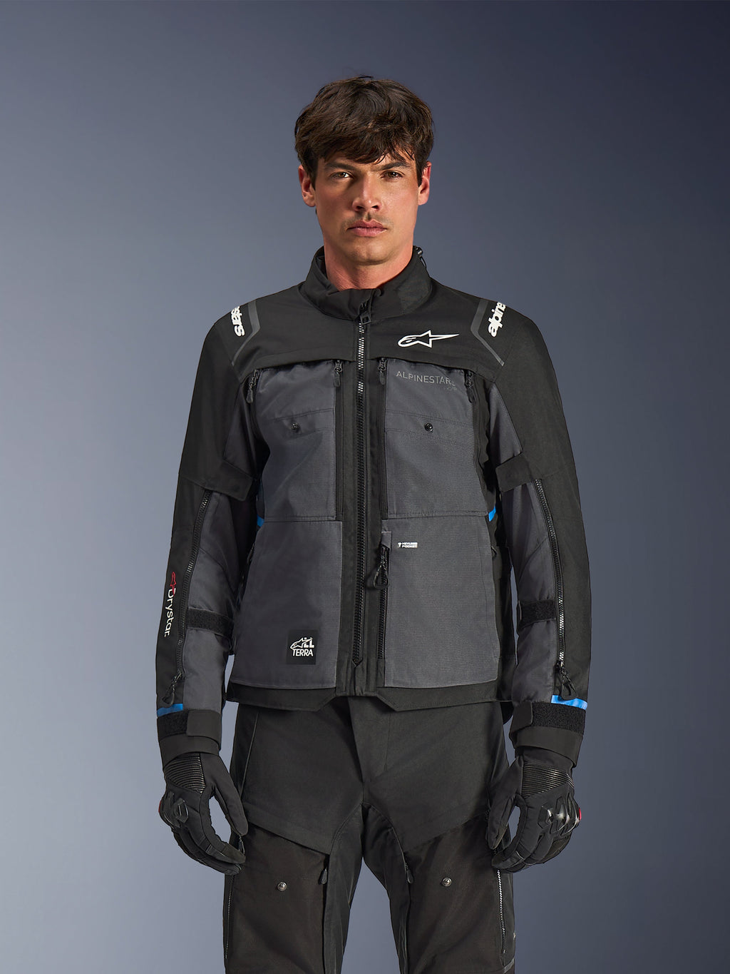 Alpinestars Cusco Drystar® jakke, motorcykel touring-jakke, sort og mørkegrå, set forfra på model, med Alpinestars-logoer på bryst og skuldre, Drystar®-branding på ærmet, teknisk multilomme-design med ventilationslynlåse, kombineret med sort køreudstyr