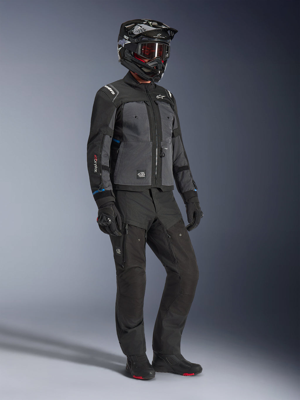 Model iført Alpinestars Cusco Drystar®-jakke i sort og mørkegrå, kombineret med komplet motorcykeludstyr herunder sort hjelm, matchende tekniske bukser, handsker og støvler, med ripstop- og softshell-konstruktion til vej- og adventure-touring