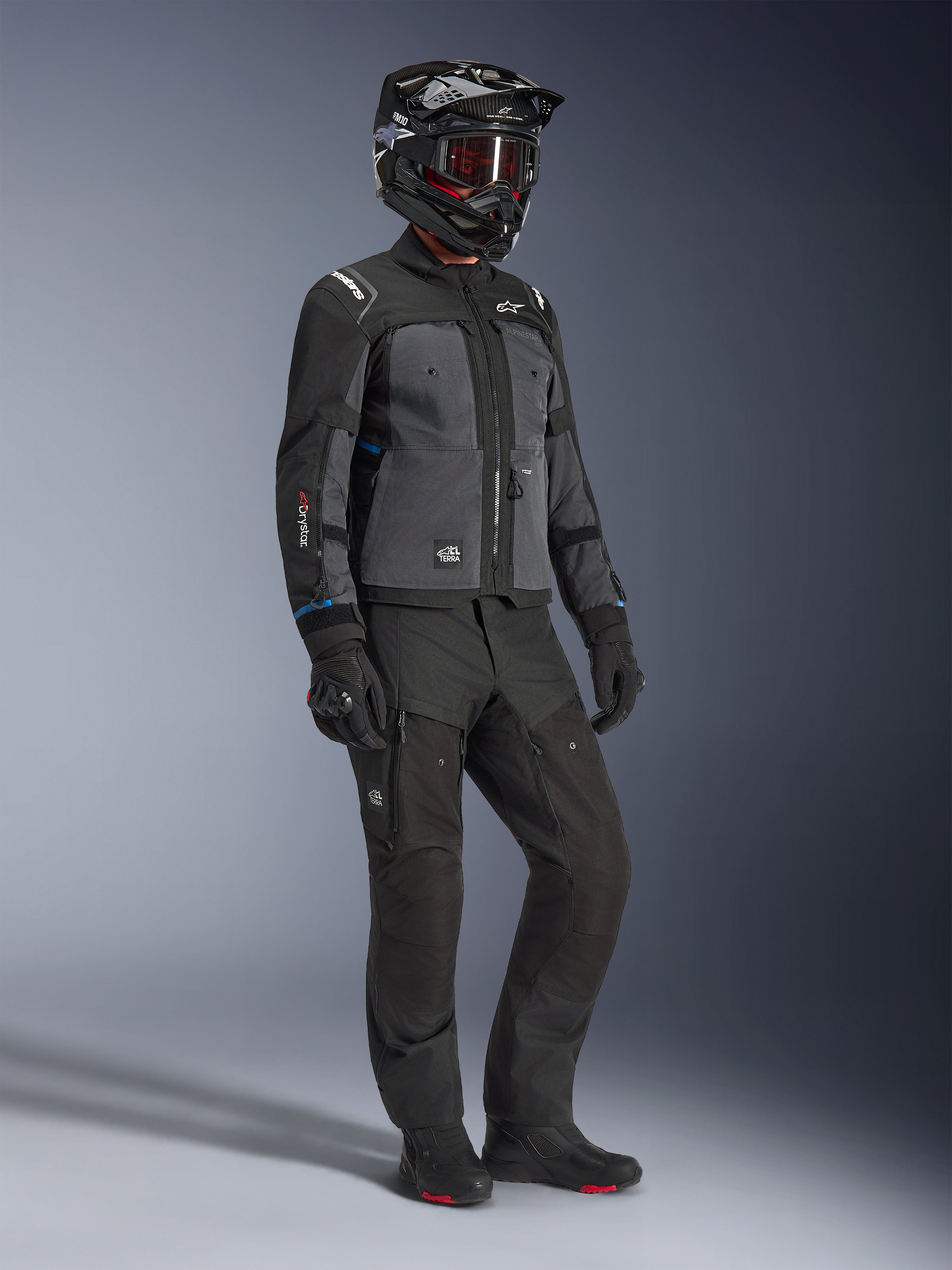 Model iført Alpinestars Cusco Drystar®-jakke i sort og mørkegrå, kombineret med komplet motorcykeludstyr herunder sort hjelm, matchende tekniske bukser, handsker og støvler, med ripstop- og softshell-konstruktion til vej- og adventure-touring