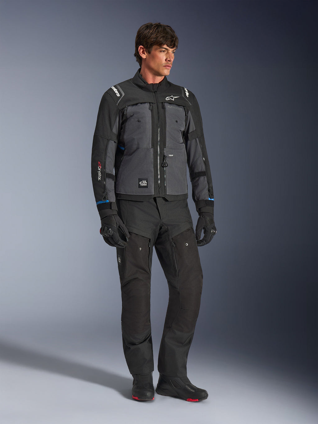 Alpinestars Cusco Drystar® jakke i sort og mørkegrå, teknisk motorcykel touring-jakke med flerfarvede paneler, båret med matchende sorte kørebukser og handsker, designet til vej- og adventure-touring.
