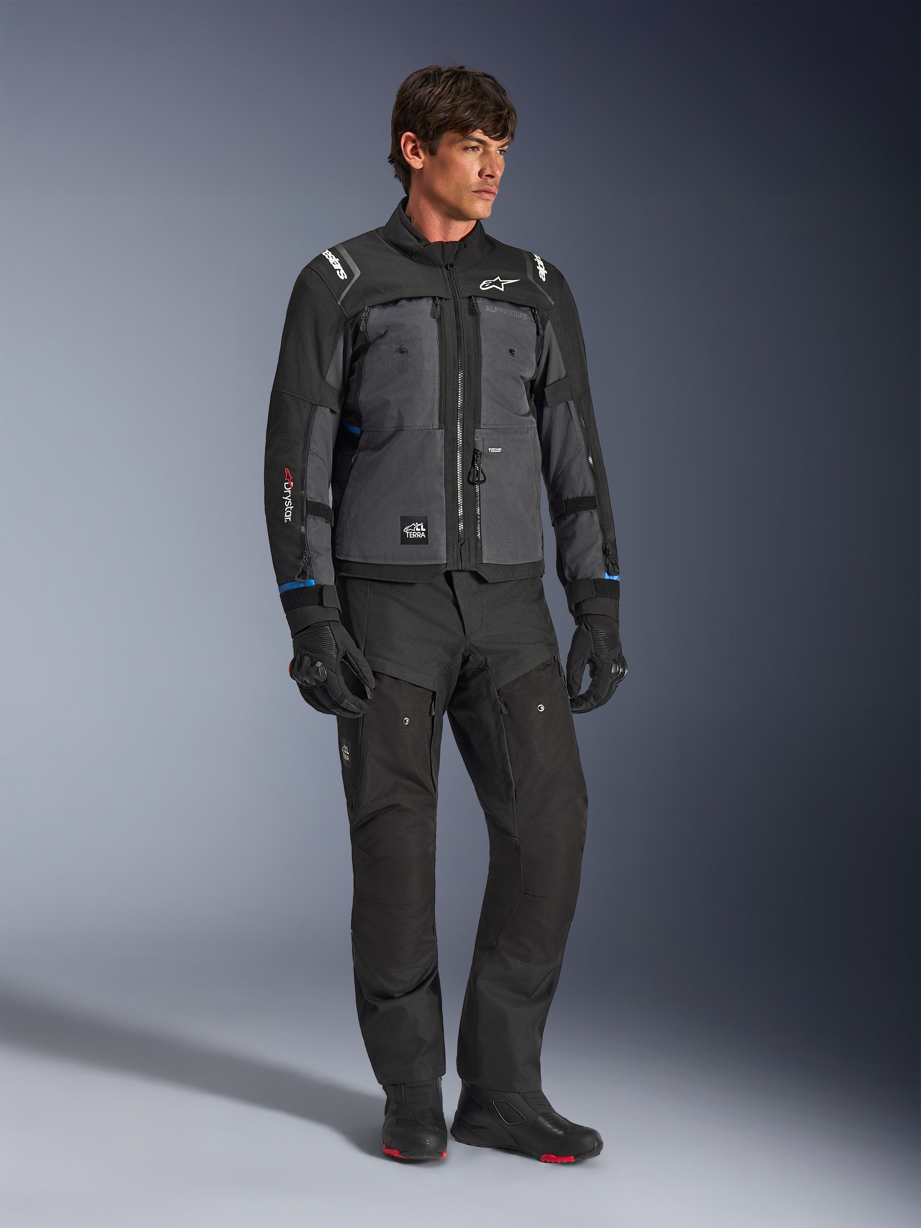 Alpinestars Cusco Drystar® jakke i sort og mørkegrå, teknisk motorcykel touring-jakke med flerfarvede paneler, båret med matchende sorte kørebukser og handsker, designet til vej- og adventure-touring.
