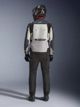 Motorcycle rider seen from behind wearing the Alpinestars Cusco Drystar® Jacket in Ice Gray, Mid Gray, and Deep Gray, featuring a large back ventilation panel and Alpinestars branding, paired with black riding pants and a black helmet, adventure touring motorcycle apparel