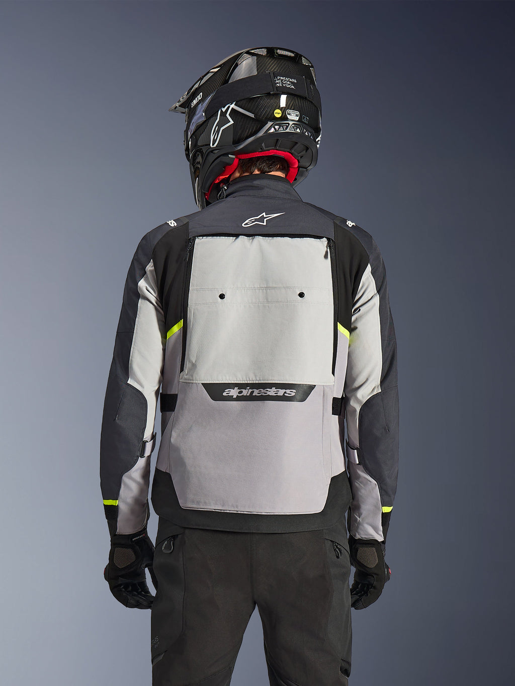 Alpinestars Cusco Drystar®-jakke, set bagfra, Ice Gray, Mid Gray og Deep Gray, med stort ventilationspanel på ryggen og neongule detaljer, båret med sort adventure-hjelm og sorte bukser
