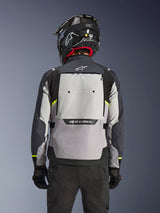 Alpinestars Cusco Drystar® Jacket, back view, Ice Gray Mid Gray and Deep Gray, featuring large rear ventilation panel and high-visibility yellow accents, worn with a black adventure helmet and black pants.