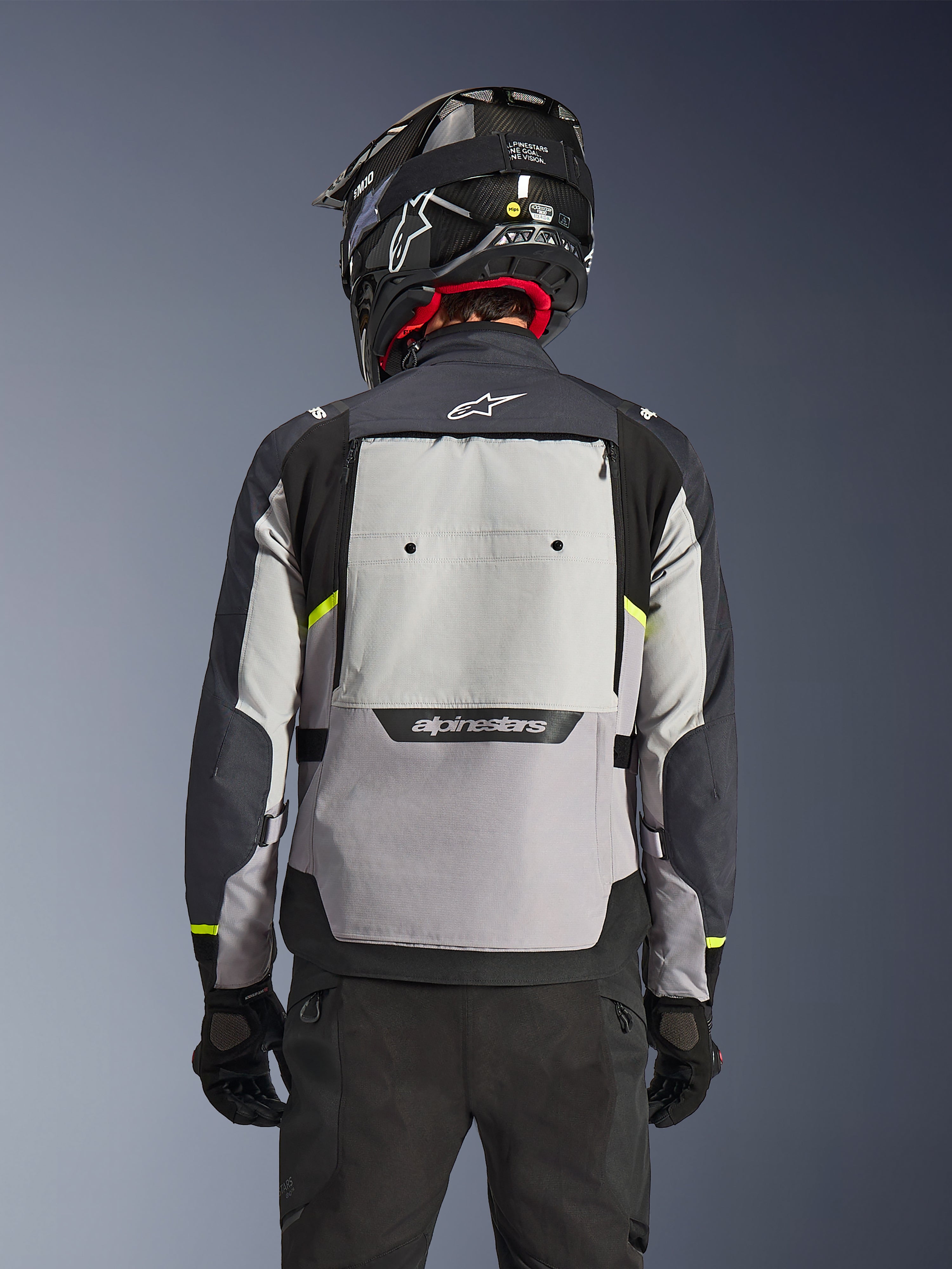 Alpinestars Cusco Drystar®-jakke, set bagfra, Ice Gray, Mid Gray og Deep Gray, med stort ventilationspanel på ryggen og neongule detaljer, båret med sort adventure-hjelm og sorte bukser