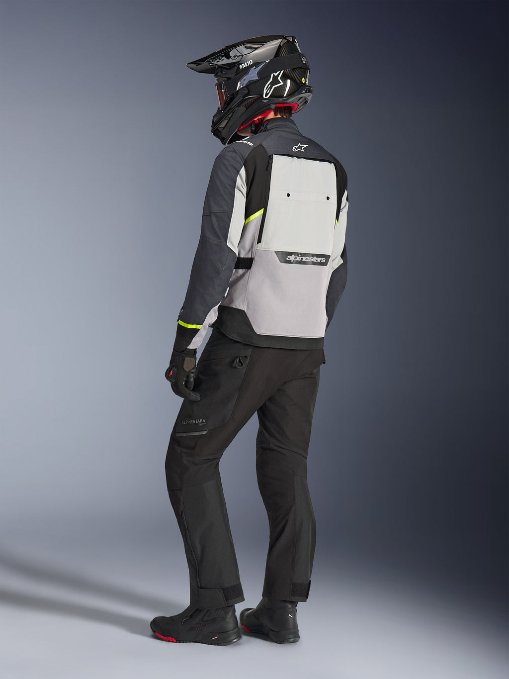 Alpinestars Cusco Drystar® jakke i Ice Gray, Mid Gray og Deep Gray, set bagfra på en kører. Har fluorescerende gule detaljer, et stort ventilationspanel på ryggen med branding og en slidstærk tekstilkonstruktion. Vist sammen med sorte motorcykelbukser og en adventure-hjelm for et komplet touring-look.