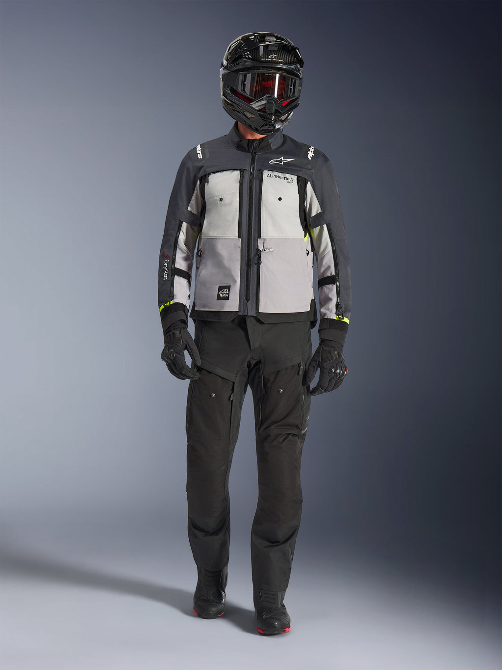 Alpinestars Cusco Drystar® jakke, Ice Gray Mid Gray Deep Gray, adventure-motorcykeljakke båret med sorte kørebukser, sorte handsker og en sort hjelm med goggles, med farveopdelte grå paneler og tekniske detaljer til vej- og adventure-touring