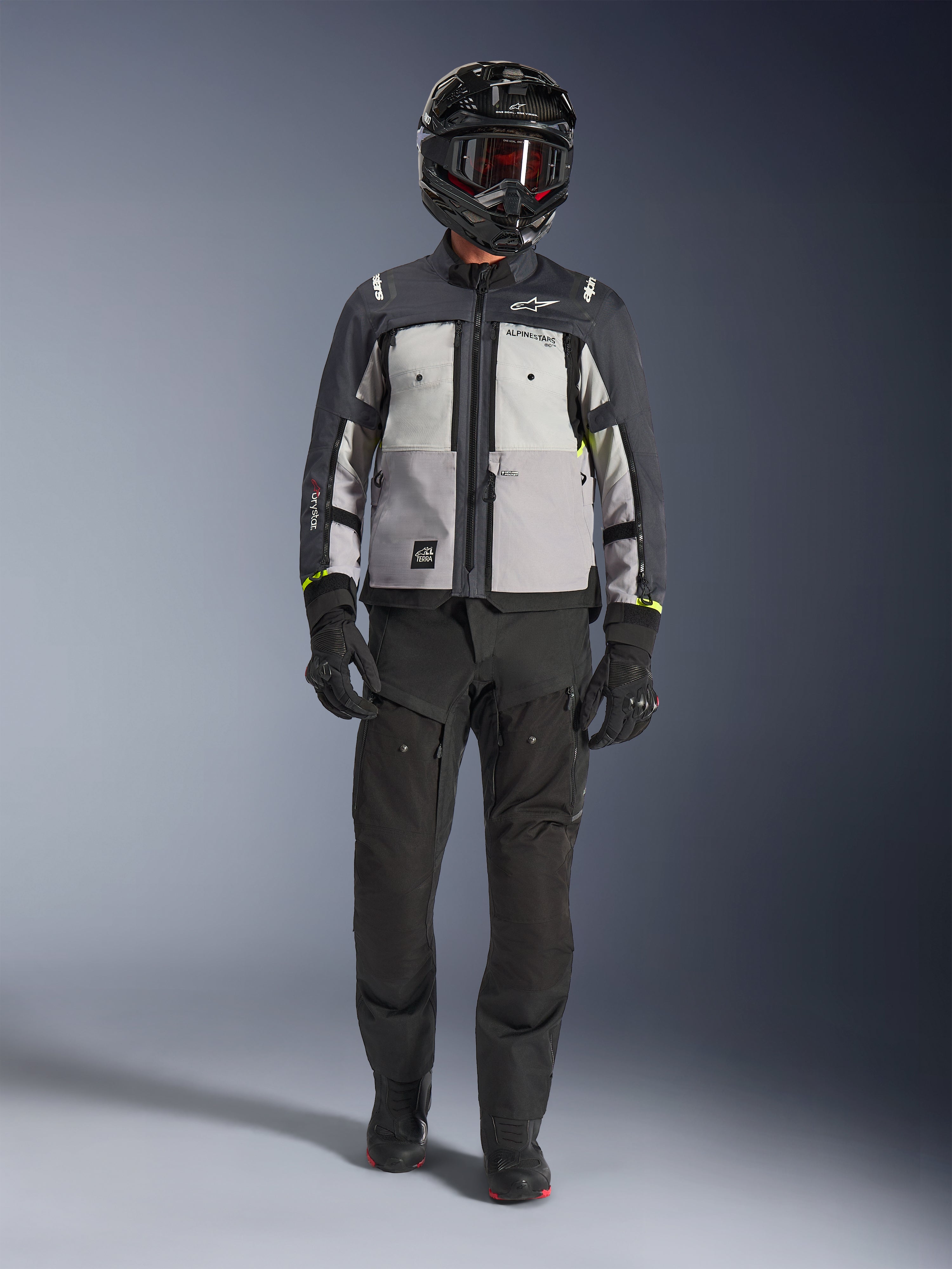 Alpinestars Cusco Drystar® jakke, Ice Gray Mid Gray Deep Gray, adventure-motorcykeljakke båret med sorte kørebukser, sorte handsker og en sort hjelm med goggles, med farveopdelte grå paneler og tekniske detaljer til vej- og adventure-touring