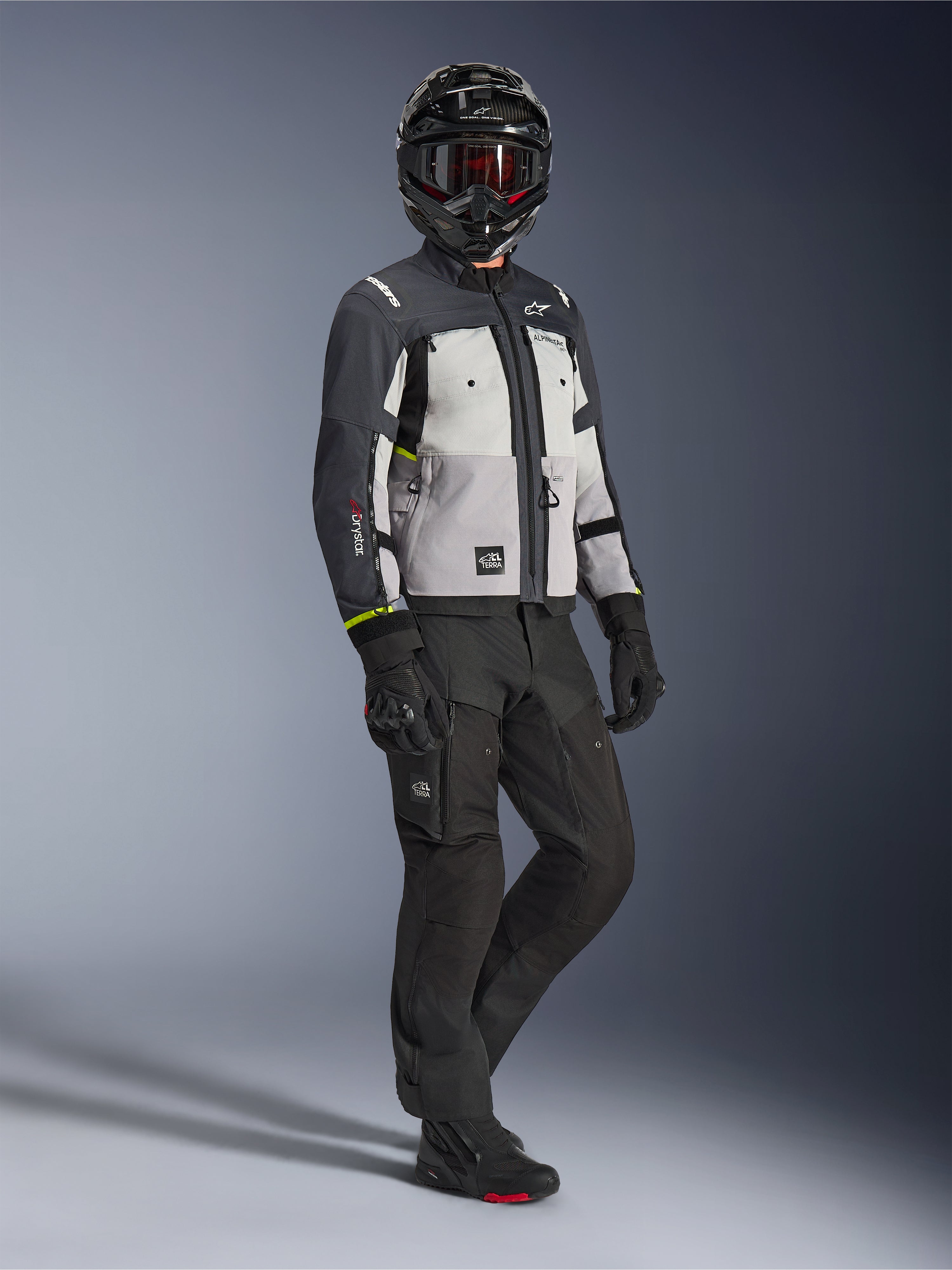 Alpinestars Cusco Drystar® jakke i Ice Gray Mid Gray Deep Gray, fuldkropsbillede af en kører i komplet adventure-udstyr, inklusiv sort hjelm med røde goggles, matchende sorte bukser og handsker, tekstil-motorcykeljakke med direkte ventilationspaneler og vandtæt membran