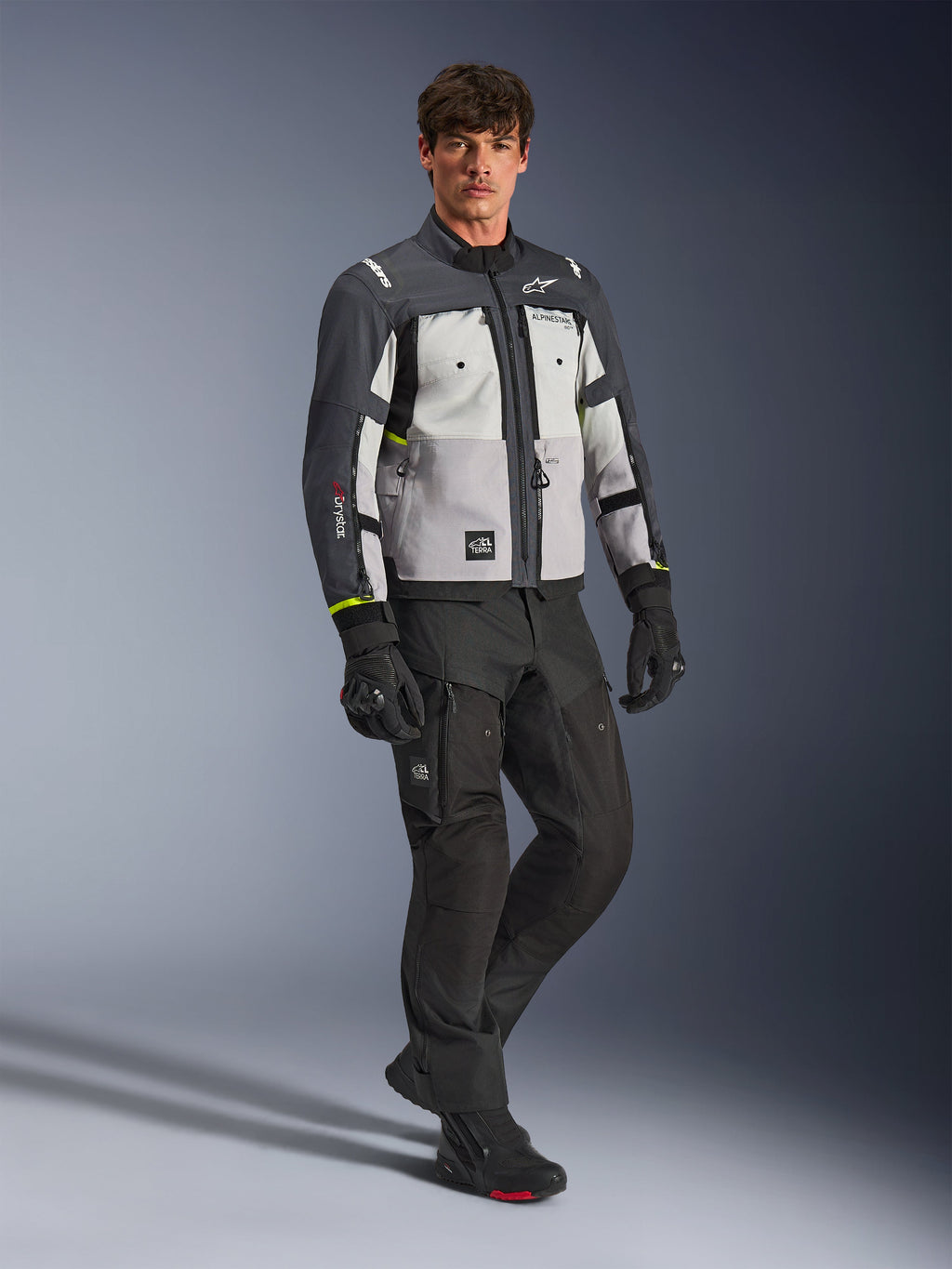 Alpinestars Cusco Drystar® jakke, adventure-motorcykeljakke, Ice Gray, Mid Gray og Deep Gray, bæres af en model med sorte bukser og handsker, flerfarvede grå paneler med slidstærk tekstilkonstruktion, med lynlåsventilation og Alpinestars-branding, professionel studiefotografering af udstyr til landevejs- og adventurekørsel
