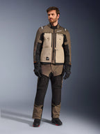 Alpinestars Cusco Drystar®-jakke i Walnut Aluminum Black, båret af en mandlig kører med matchende adventure touring-bukser, sorte handsker og støvler, med sandfarvede brystpaneler, sorte ærmer med diskrete orange detaljer og funktionelle ventilationslynlåse til motorcykelkørsel på vej.