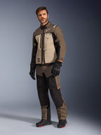 Alpinestars Cusco Drystar® jakke i Walnut Aluminum Black, båret af en mandlig model med matchende motorcykelbukser og handsker, adventure-touring design med sandfarvede brystpaneler og sorte detaljer.