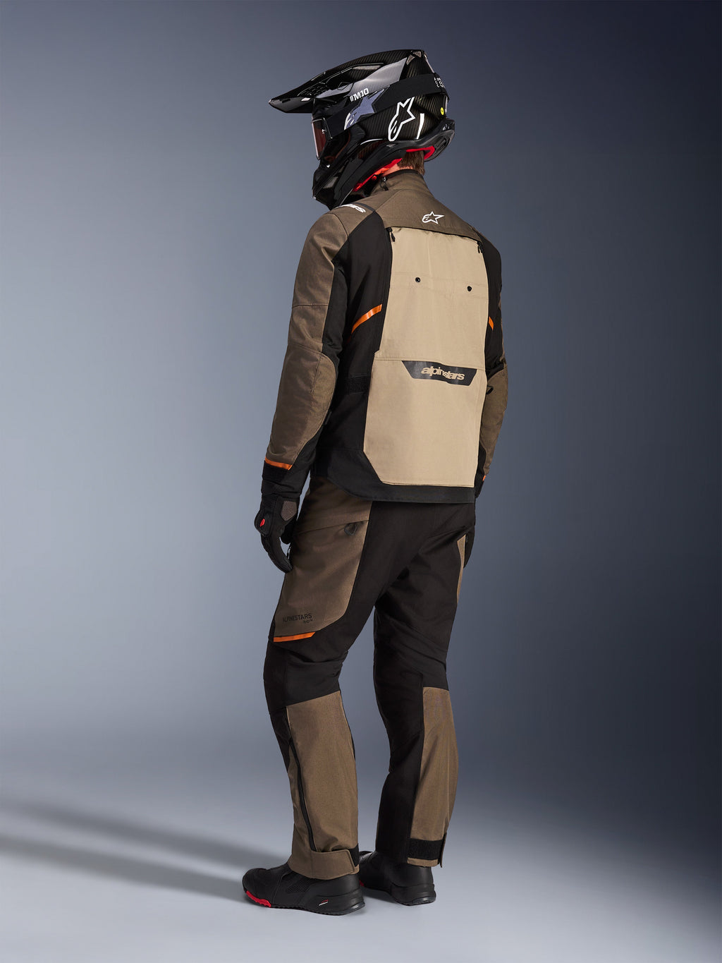 Alpinestars Cusco Drystar® jakke, adventure touring-jakke, Walnut Aluminum Black, set bagfra med lysebrunt rygpanel og orange detaljer, båret med matchende bukser og sort kulfiberhjelm.