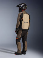 Alpinestars Cusco Drystar® jakke, adventure touring-jakke, Walnut Aluminum Black, set bagfra med lysebrunt rygpanel og orange detaljer, båret med matchende bukser og sort kulfiberhjelm.