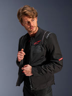 Alpinestars ST-2 Air Jakke, sort, sommer-motorcykel-touringjakke med store mesh-paneler, med et rødt Astars-logo og 'Alpinestars Exploration Equipment'-tekst på brystet, moderne teknisk design til luftstrøm og beskyttelse, båret af en model